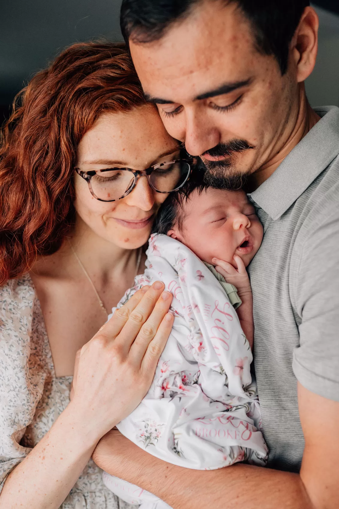 Parents holding a brand new baby in between them, snuggling her gently during home newborn photos.