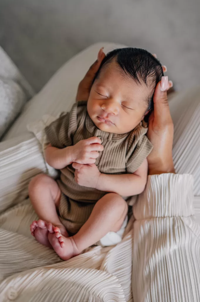 Newborn baby boy in mom's lap. Her hands are curled around his tiny baby head.