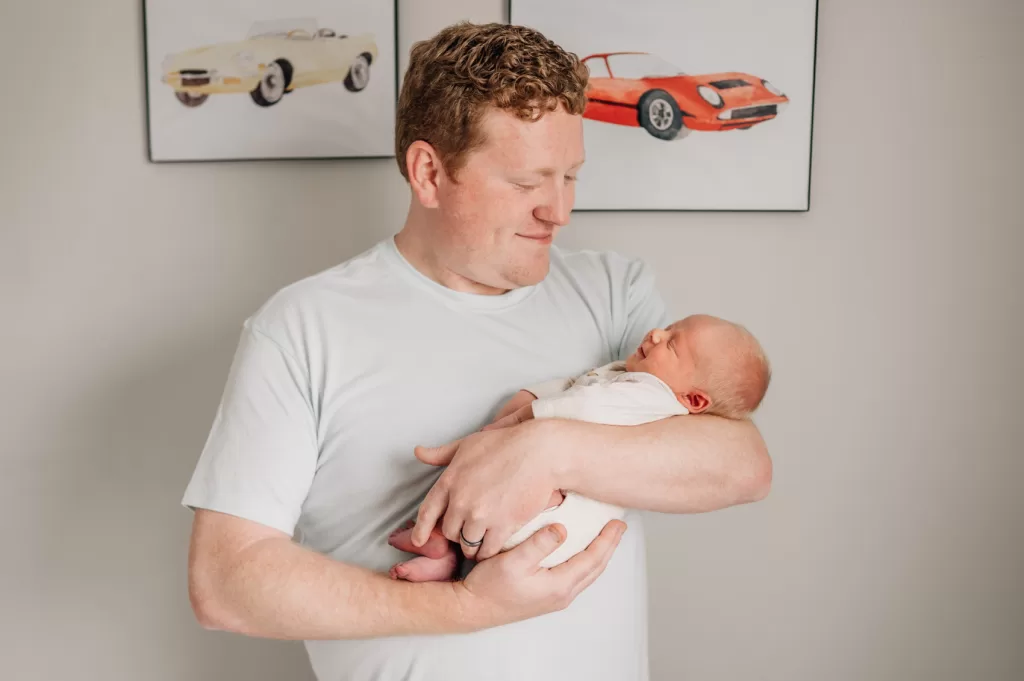 Dad holding his newborn baby son smiling down at him.