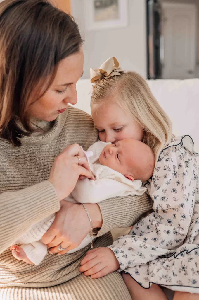 Mom holding newborn and a 4 year old daughter snuggling into her arm