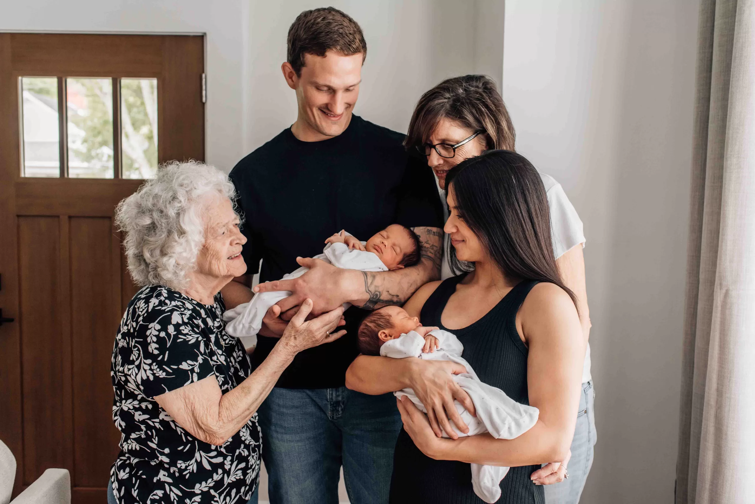 Grandma and Great Grandma admire twin newborn girls sleeping in parents arms