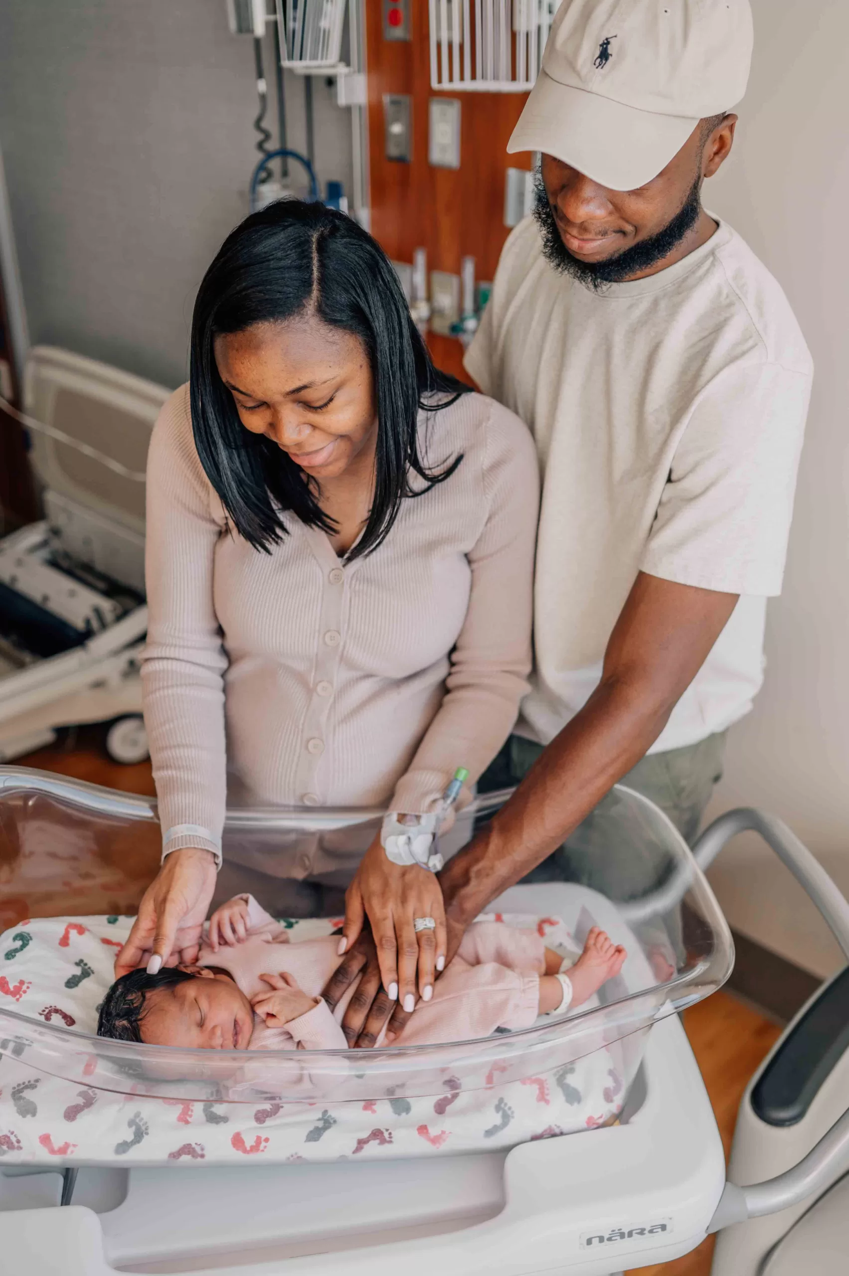 New mom and dad stand over and lay hands on their sleeping newborn daughter in the hospital crib