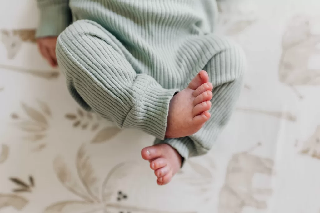 Details of a newborn baby's feet in a green onesie while laying in a crib