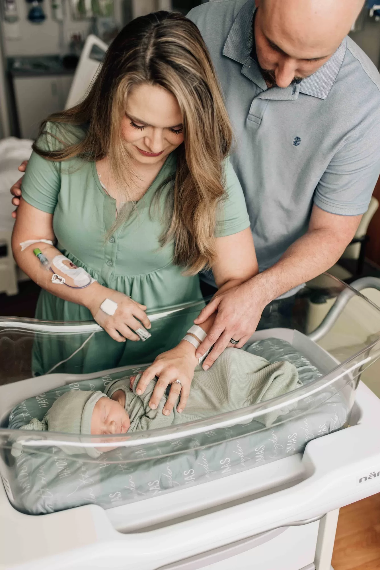 New mom and dad stand over their sleeping newborn in the hospital crib after using doulas in Columbia, SC