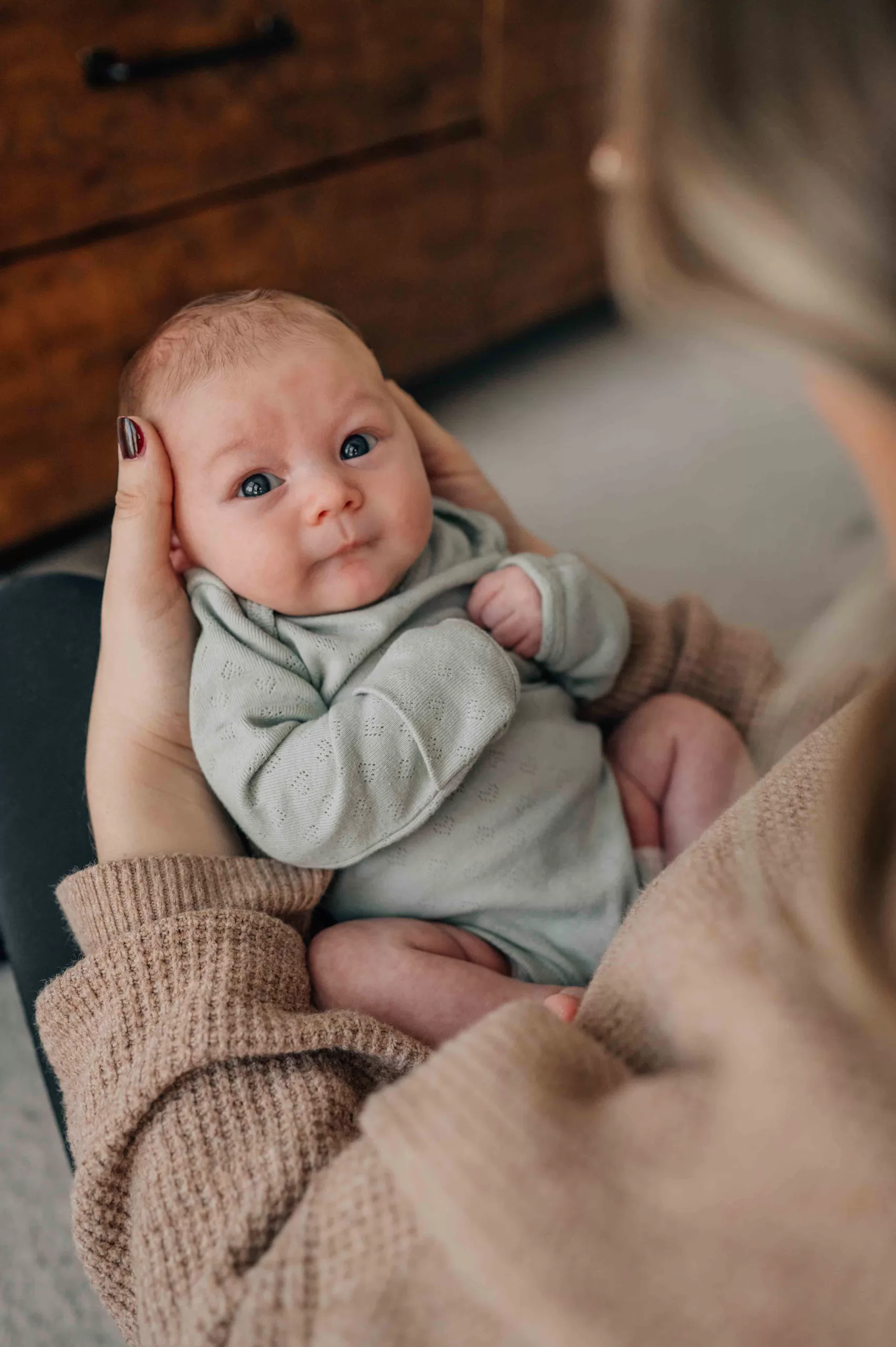 An awake newborn in a green onesie looks up to mom while laying in her lap and hands after meeting midwives in Columbia, SC