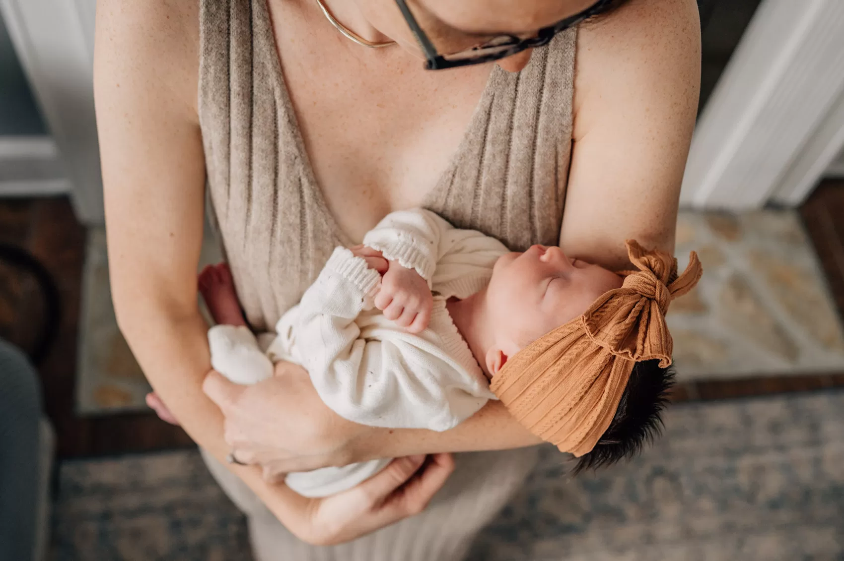 A new mom gazes down to her newborn daughter sleeping in her arms with a large brown bow