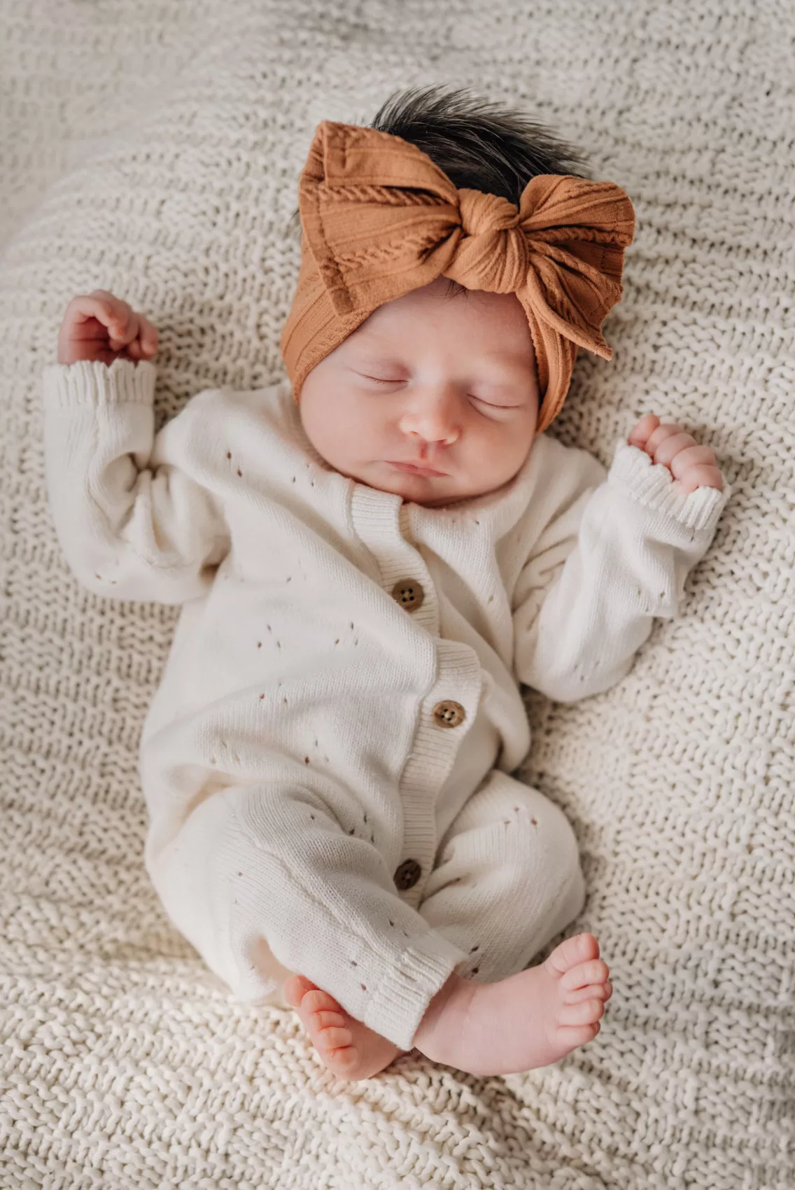 A newborn baby girl sleeping on a bed in a white onesie and brown bow thanks to a sleep coach in Columbia, SC