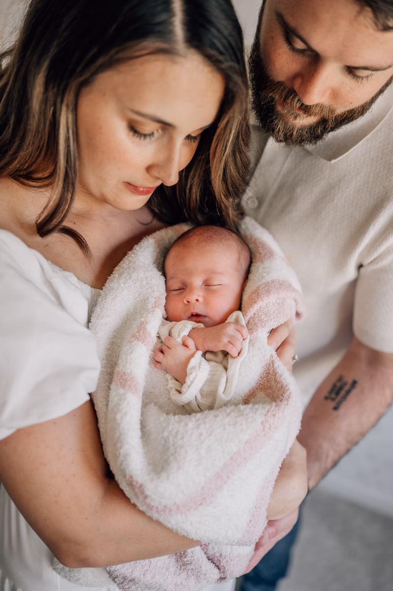 New mom and dad gaze down at their sleeping baby girl wrapped in a blanket in mom's arms thanks to postpartum doulas in fort mill, SC